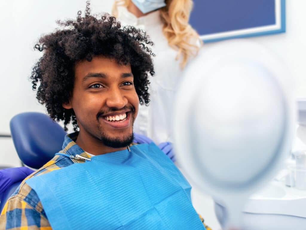 How Long Do Dental Implants Last? What Affects Their Lifespan? 1 Smiling patient seated in a dental chair during a dental implant consultation.
