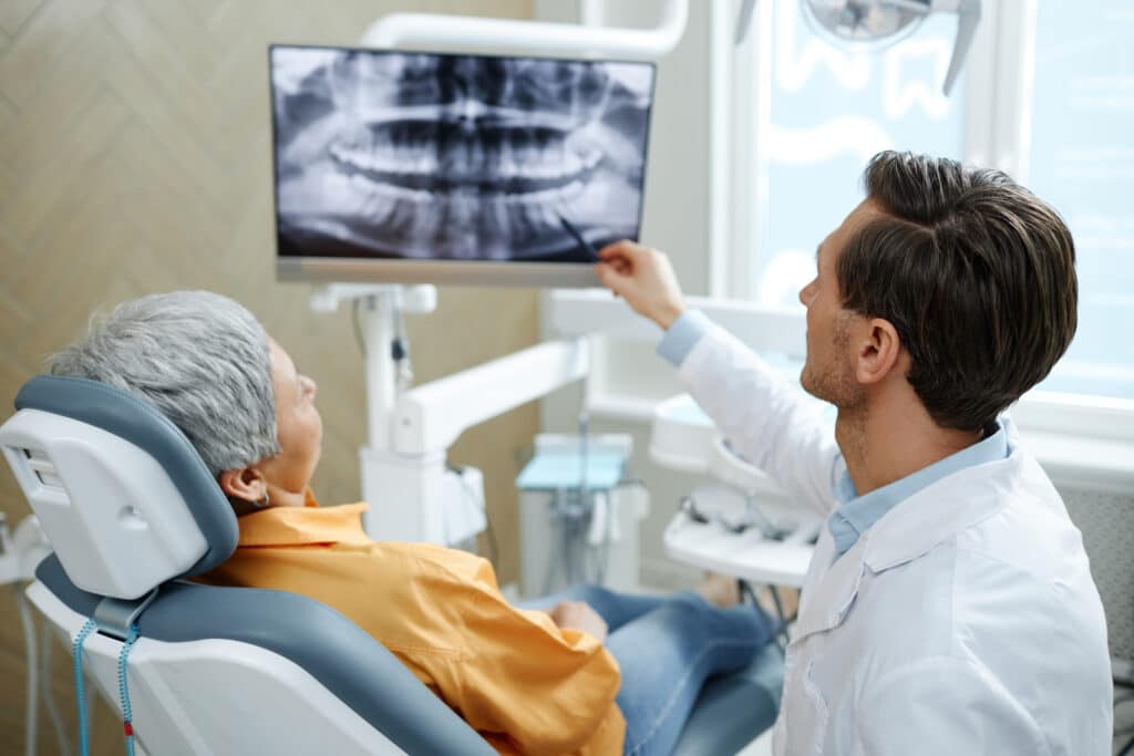 What Are the Signs of Dental Implant Failure, and Can a Failing Implant Be Saved? 1 Dentist reviewing a panoramic dental X-ray with a patient during a dental implant evaluation.
